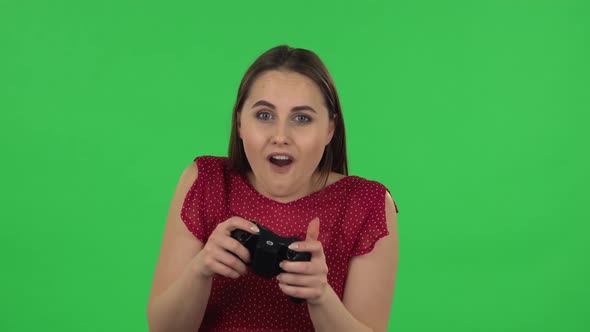 Portrait of Tender Girl in Red Dress Is Playing a Video Game Using a Wireless Controller and Losing