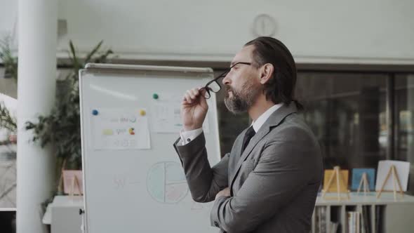 Confident Businessman Taking Off His Glasses and Looking Away Wearing an Elegant Navy Suit Standing