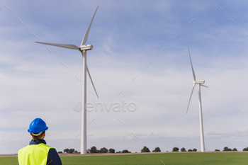 tors in a wind farm. Engineer in work clothes and personal protective equipment looking at clean and non-polluting energy installations.