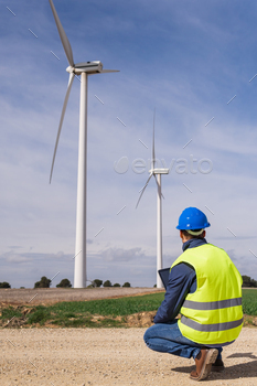 al tablet in a zero emission renewable energy facility, with electric wind turbines in the background. Climate change and alternative energy concept.