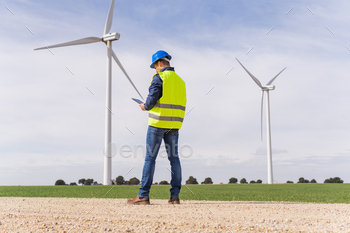 ctor, from the back looking at his digital tablet in a field of wind turbines. Increase in energy prices in the market and alternative energies.