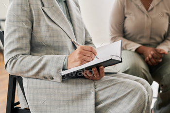 Female psychoanalyst in grey suit holding pen over page of open notebook