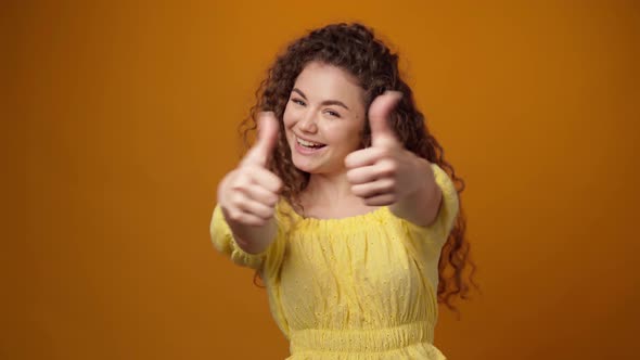 Young Curly Haired Woman Showing Thumbs Up Sign Against Yellow Background