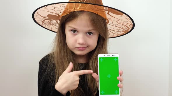 Little Girl in Witch Halloween Costume Shows the Phone with a Green Screen