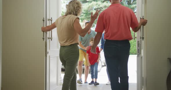 Happy caucasian grandparents opening door and greeting their family