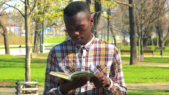 A Young Black Man Reads a Book in a Park on a Sunny Day