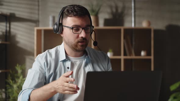 Young Male Trainer Coach Teacher in Eyeglasses Wearing Headphones Looking at Computer Screen Giving