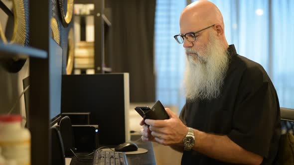 Mature Bald Bearded Man Using Phone While Working From Home