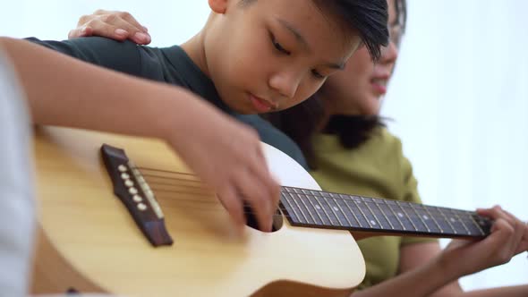 Asian mother embraces son, Asian boy playing guitar and mother embrace on the sofa