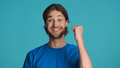 Cheerful man raising fist celebrating success isolated on blue background. Guy feeling like winner - PhotoDune Item for Sale