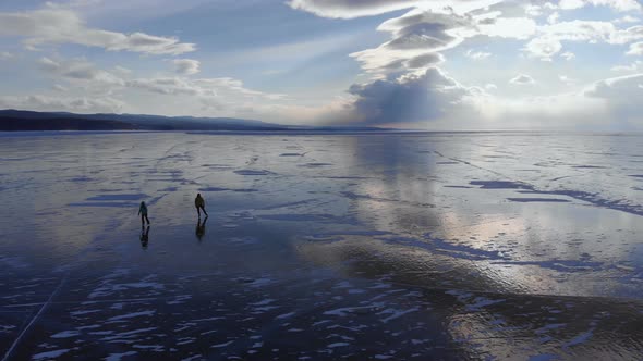 Silhouettes of Two People Skating on the Ice of the Frozen Sea at Sunset