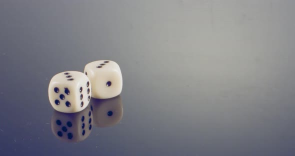 Slow motion macro shot of white dice falling and rolling on reflective surface