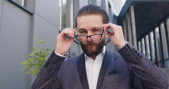 man in business suit which putting on his glasses while loooking at camera with nice smile