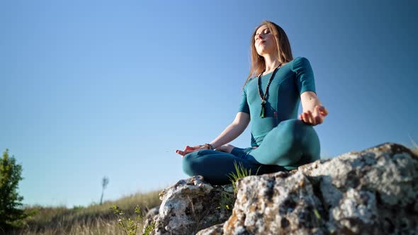 Concentrated Woman in Lotus Pose Doing Meditation on High Cliff Above Water