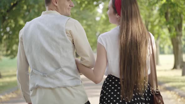 Back View of Loving Romantic Young Couple Strolling in Sunny Park and Talking. Handsome Caucasian