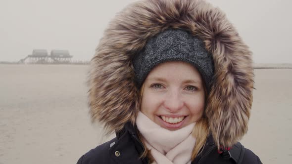 Young woman standing in the wind of a barren landscape, protected from the freezing cold with a fur