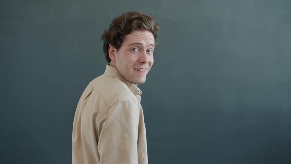 Portrait of Goodlooking Young Man Turning and Smiling Looking at Camera on Gray Background