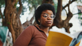 African curly-haired girl reading a book outdoors, wearing glass - PhotoDune Item for Sale