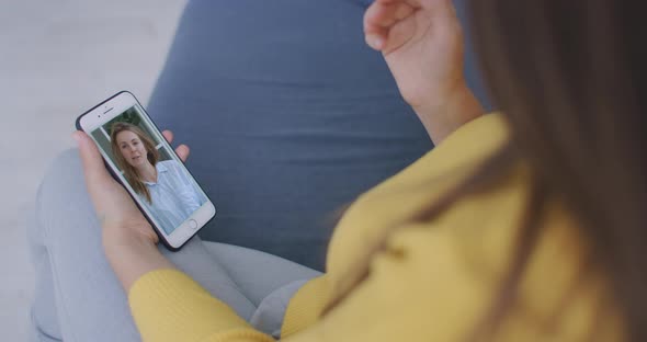 Curly Young Woman Having Video Chat with Friends Using Mobile Phone Camera While Lying on Bed