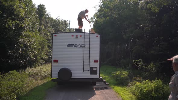 Elderly man sweeping the top of his RV with a broom after boondocking.