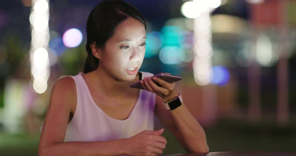 Woman sending audio message on cellphone at night