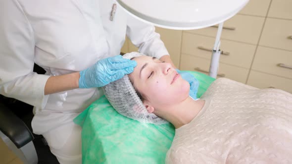 Beautician Gently Cleaning Skin of Young Woman Lying on Medical Couch in Beauty Clinic