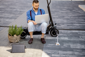 Man charges laptop with solar panels while sitting on electric scooter outdoors