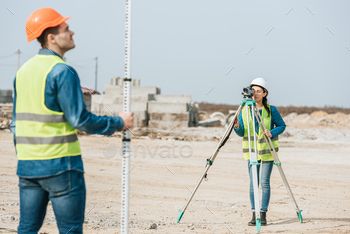 Selective focus of surveyors using digital level and ruler on construction site