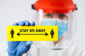 Medical worker in personal protective equipment holding yellow "STAY 6ft AWAY" sign - PhotoDune Item for Sale