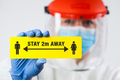 Medical worker in personal protective equipment holding yellow "STAY 2m AWAY" sign - PhotoDune Item for Sale