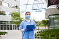 Head of care wearing personal protective equipment holding folder standing in front of nursing home - PhotoDune Item for Sale