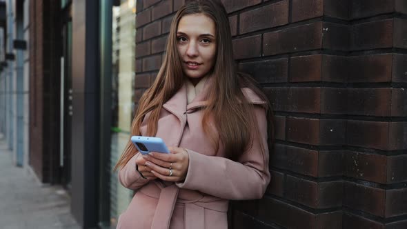 Pretty young long hair woman in a coat using mobile phone at the city