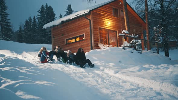 Best Friends Sliding on the Sleds Downhill in Front of the Wooden House