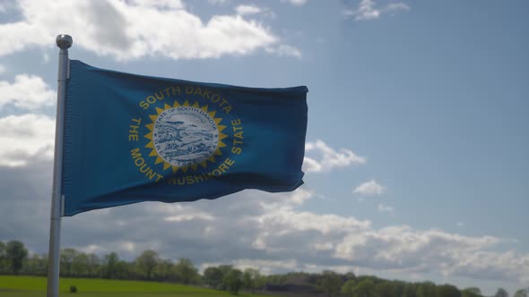 South Dakota Flag on a Flagpole Waving in the Wind Blue Sky Background