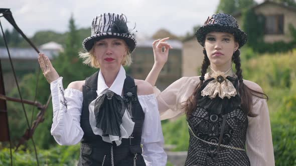 Serious Adult and Young Women Looking at Camera Opening and Closing One Eye with Hand