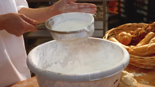 Female baker sifting flour through a sieve