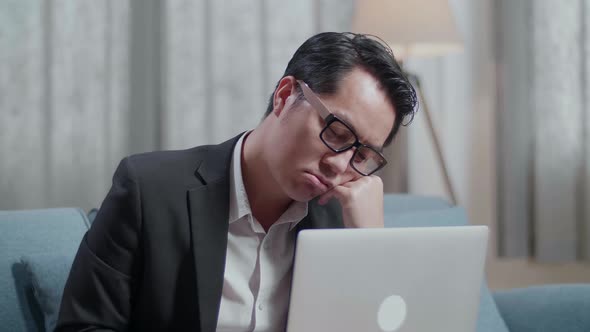 Asian Businessman In Jacket And Shorts Holding His Cheek And Sleeping While Working With A Laptop