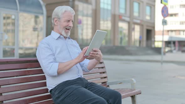 Old Man Celebrating Online Win on Tablet While Sitting Outdoor on Bench