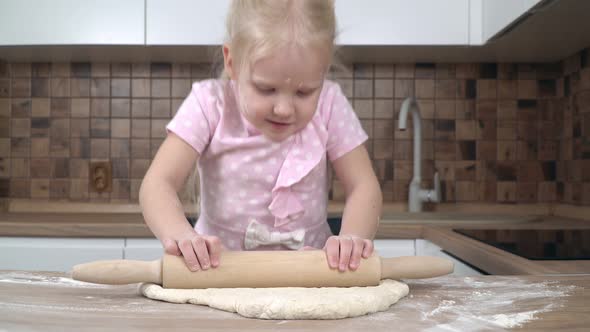 A Child in the Kitchen Rolls Out the Dough with a Rolling Pin