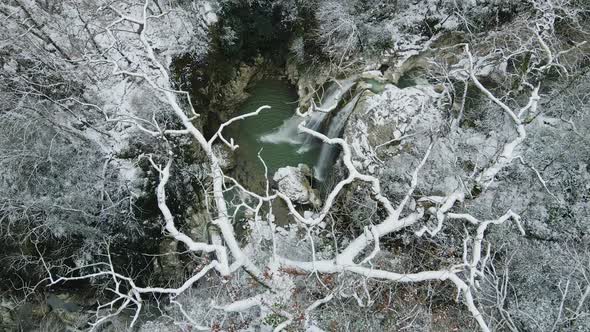 Waterfall Flowing Down From Rocks Shot Through the Branches of a Tree in Winter