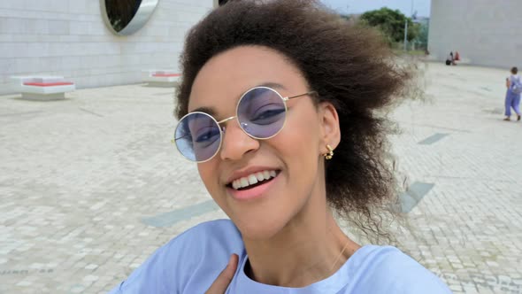 Fashionable Modern Joyful African American Curly Haired Girl with Blue Glasses Video Blogger Walks