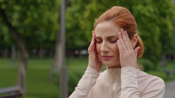 Woman suffers headache in the park, close-up face view