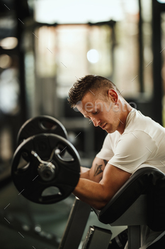 t the hard training in the gym. He is pumping up biceps muscule with heavy weight.