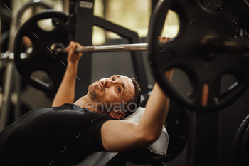 t the hard training in the gym. He is pumping up chest muscule with heavy weight.