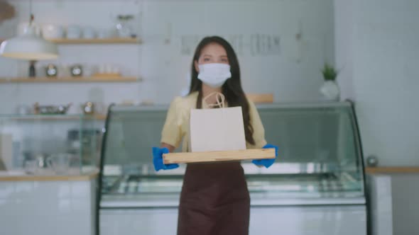 Attractive asian female cafe worker wears face mask and gloves giving takeaway food bag