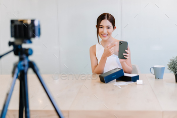 autiful young Asian woman vlogger or blogger live broadcasting review iPhone 11 pro max (midnight green) on streaming platform through digital camera, looking at camera.
