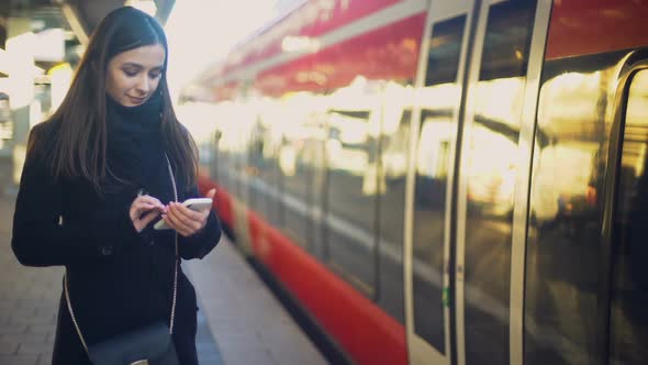 Attractive Lady Standing Near Train and Typing on Smartphone, Online Tickets