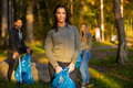 Young female volunteer in front of her team holding garbage bag at park - PhotoDune Item for Sale