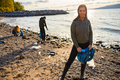 Smiling young woman cleaning beach for plastic with volunteers during beautiful sunset - PhotoDune Item for Sale