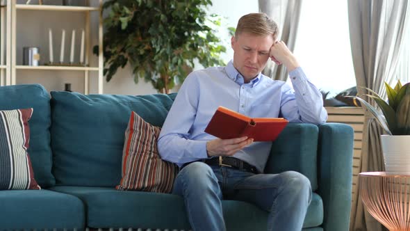 Middle Aged Man Sleeping While Reading Book Sitting on Sofa